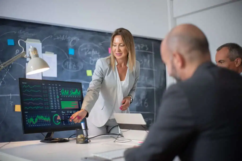 Company employees discussing market data on charts. Woman leader and two men looking at diagrams on computer screen analyzing profit growth.