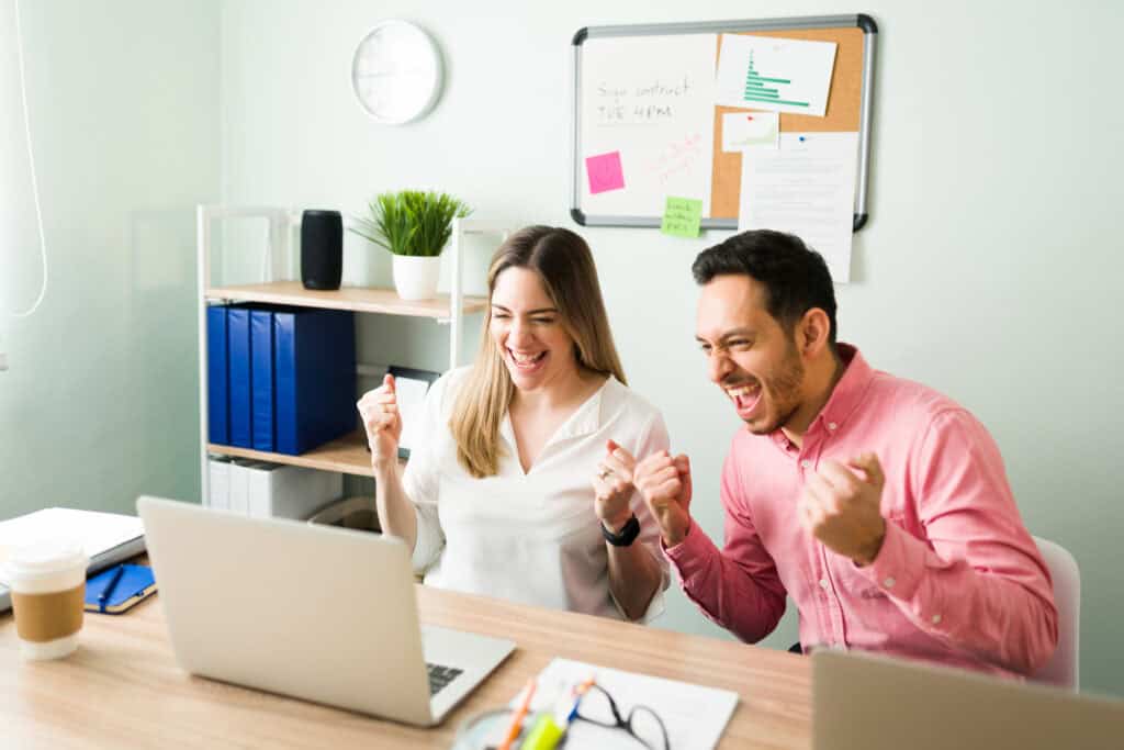 Excited colleagues cheering during an online meeting at the office, celebrating after making a work deal on a video call on their laptop