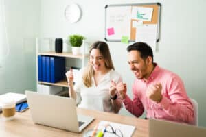 Excited colleagues cheering during an online meeting at the office, celebrating after making a work deal on a video call on their laptop