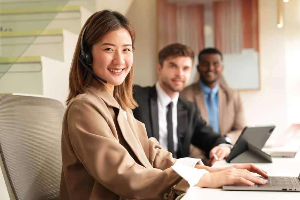 Customer contact team, woman with headset on and two men in the backround, work at an office