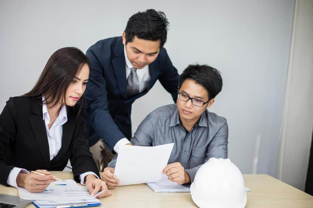 Three supplier engineers, two men and one woman, are sitting at table, looking over documents